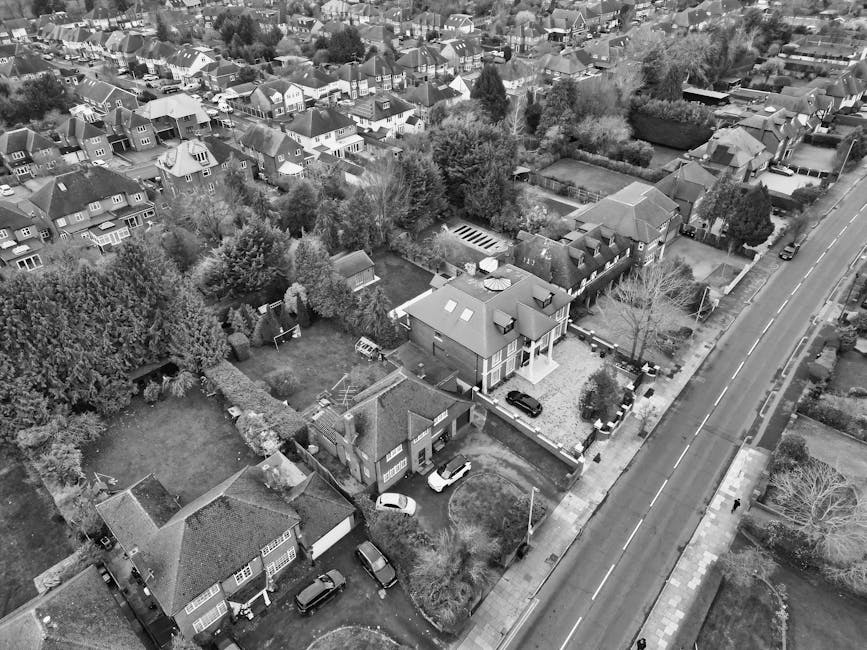 A large two-storey brick house with a red tiled roof, featuring multiple rectangular windows with dark frames, some of which are bay windows, and two prominent brick chimneys rising from the roof. The